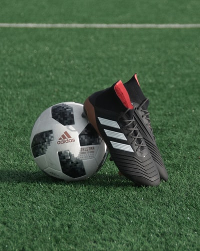 黑色阿迪达斯鞋钉靠在白色和黑色阿迪达斯足球在绿色草地上